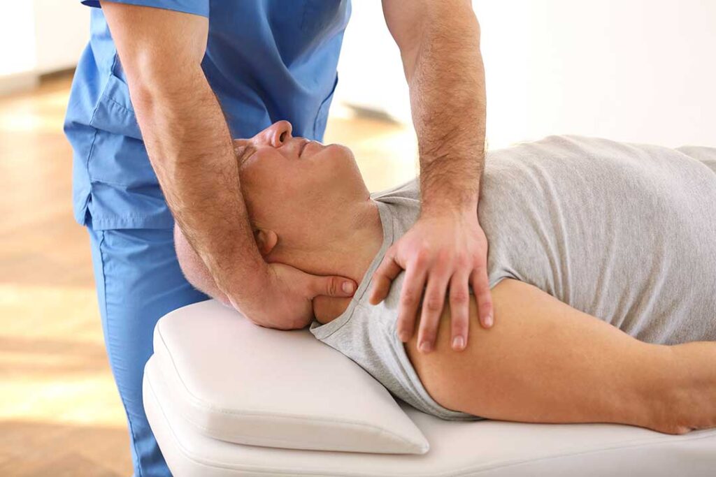 Adult performing gentle back mobility exercises beside a desk in a bright home workspace.